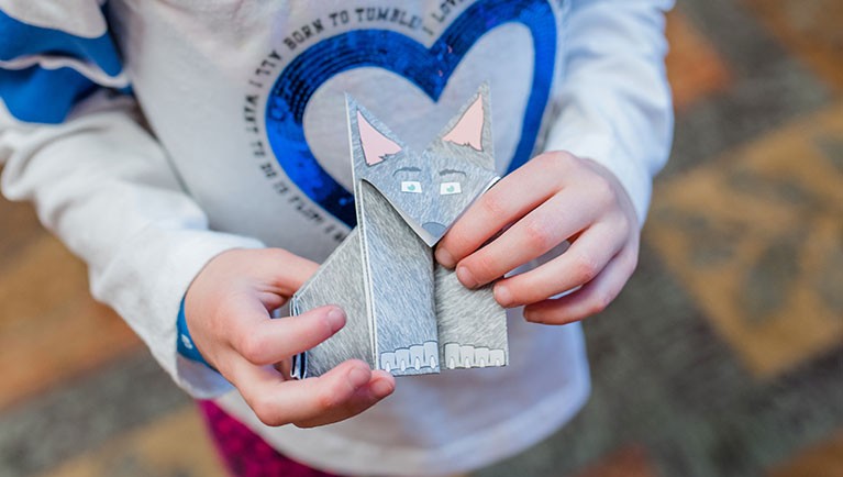 a child hold a grey origami paper wolf 